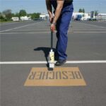 Aufsprühen von "Besucher" mit Schablone auf Parkplatz